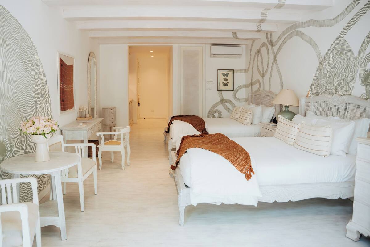 Quarto espaçoso com uma cama grande, uma escrivaninha e uma cadeira. Há uma porta que dá para outro quarto.