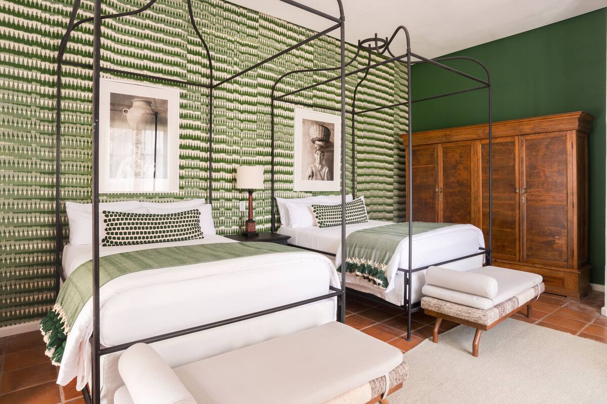 Quarto com duas camas, guarda-roupa de madeira e papel de parede estampado.