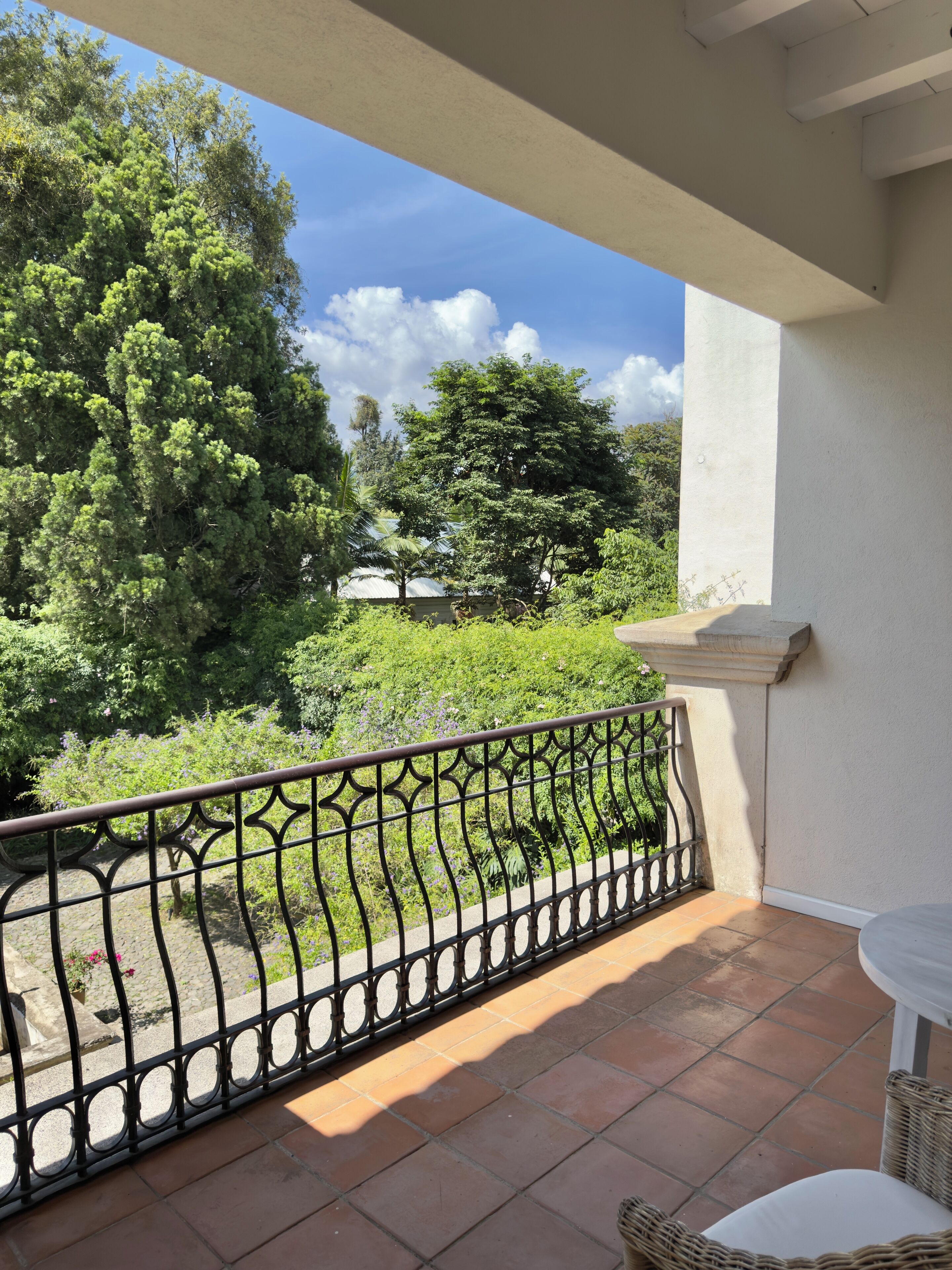 A balcony with a wrought iron railing, terracotta tiles, and a wicker chair.