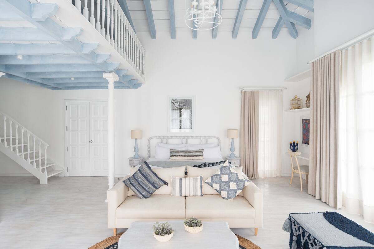 Uma sala de estar ampla com um sofá branco, uma mesa de centro com plantas, uma escada e um candelabro.