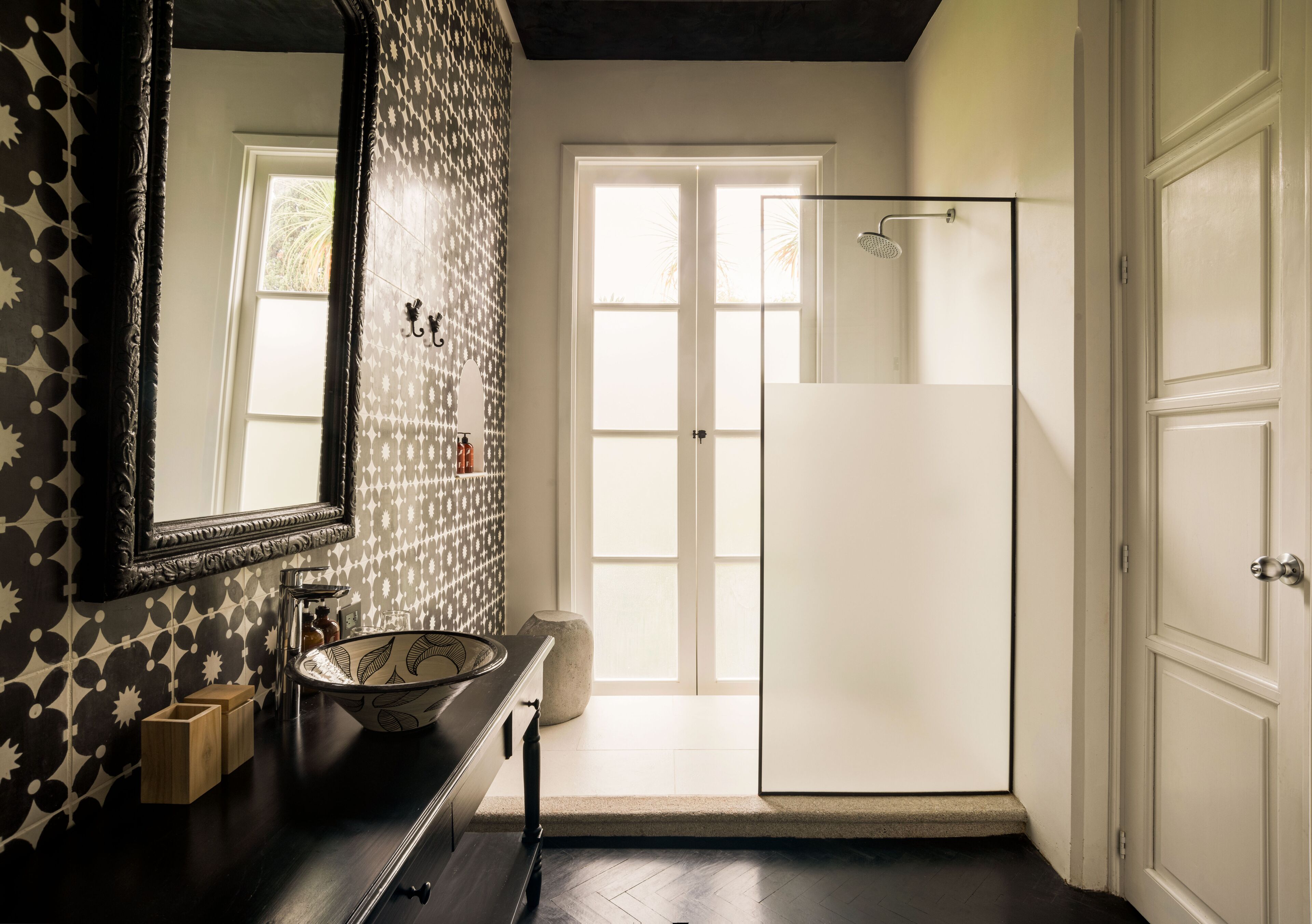 A bathroom with a large mirror, a sink, a shower, and a door leading to another room.