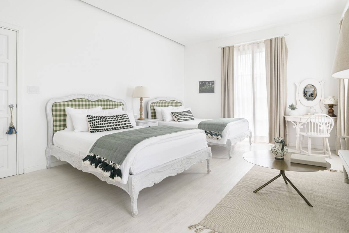 Quarto com duas camas, uma mesa de cabeceira com luminária, uma cadeira e uma mesinha com objeto decorativo.
