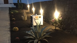 Een woestijntuin met cactussen en agaveplanten, een wit generator en een stenen muur.