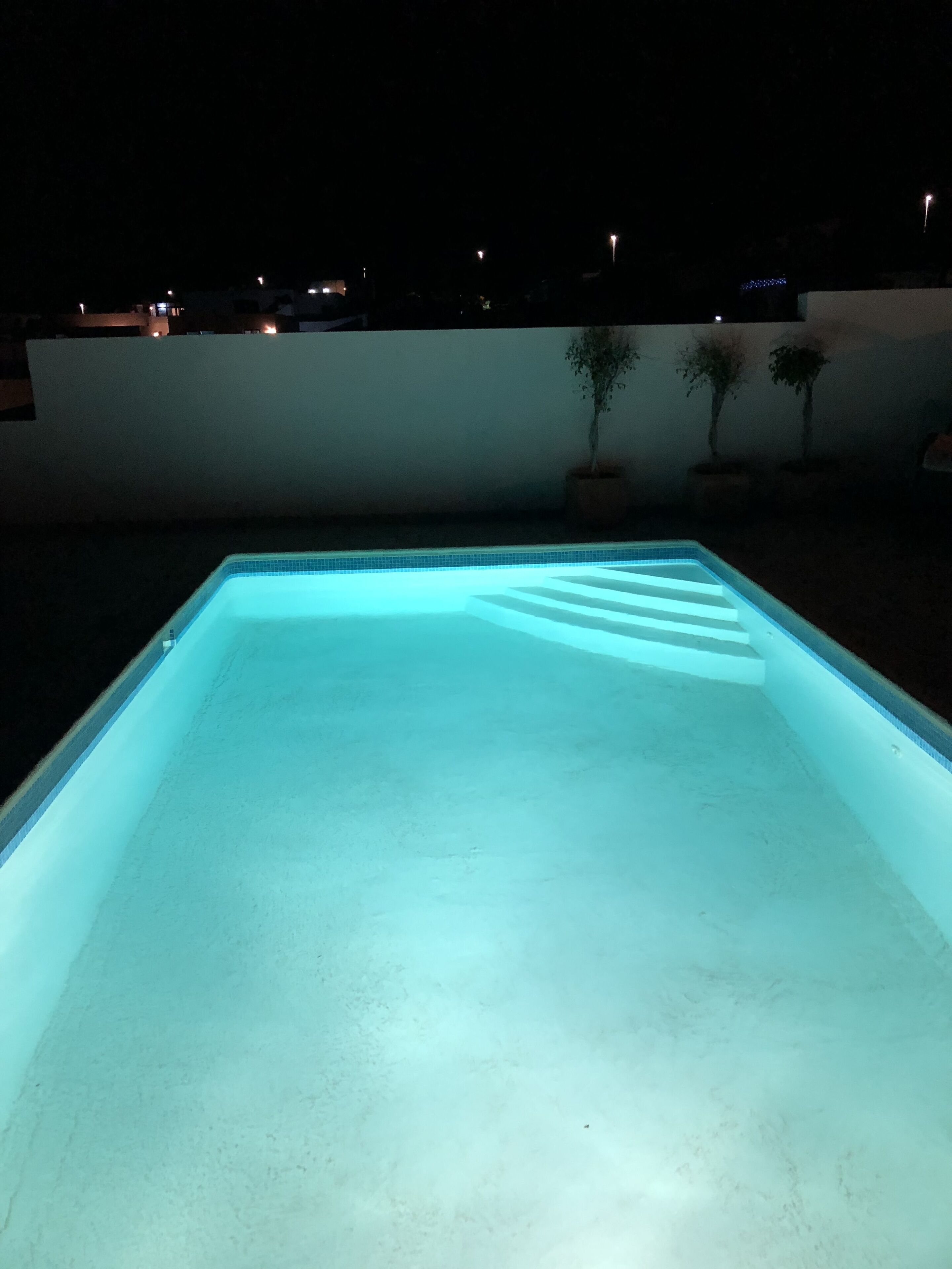 Piscina rectangular con borde de azulejos, rodeada por un muro blanco bajo.