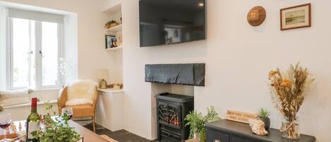 A living room with a fireplace, a television mounted on the wall, and a dining area with a table set for two.