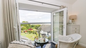 A balcony with a glass door, wicker furniture, a small table with a vase, and a view of a garden. - Sandacre Cottage (Ulverston)