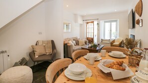 A dining area with a wooden table set for breakfast, including croissants, a glass of orange juice, and a bottle of milk. - Sandacre Cottage (Ulverston)