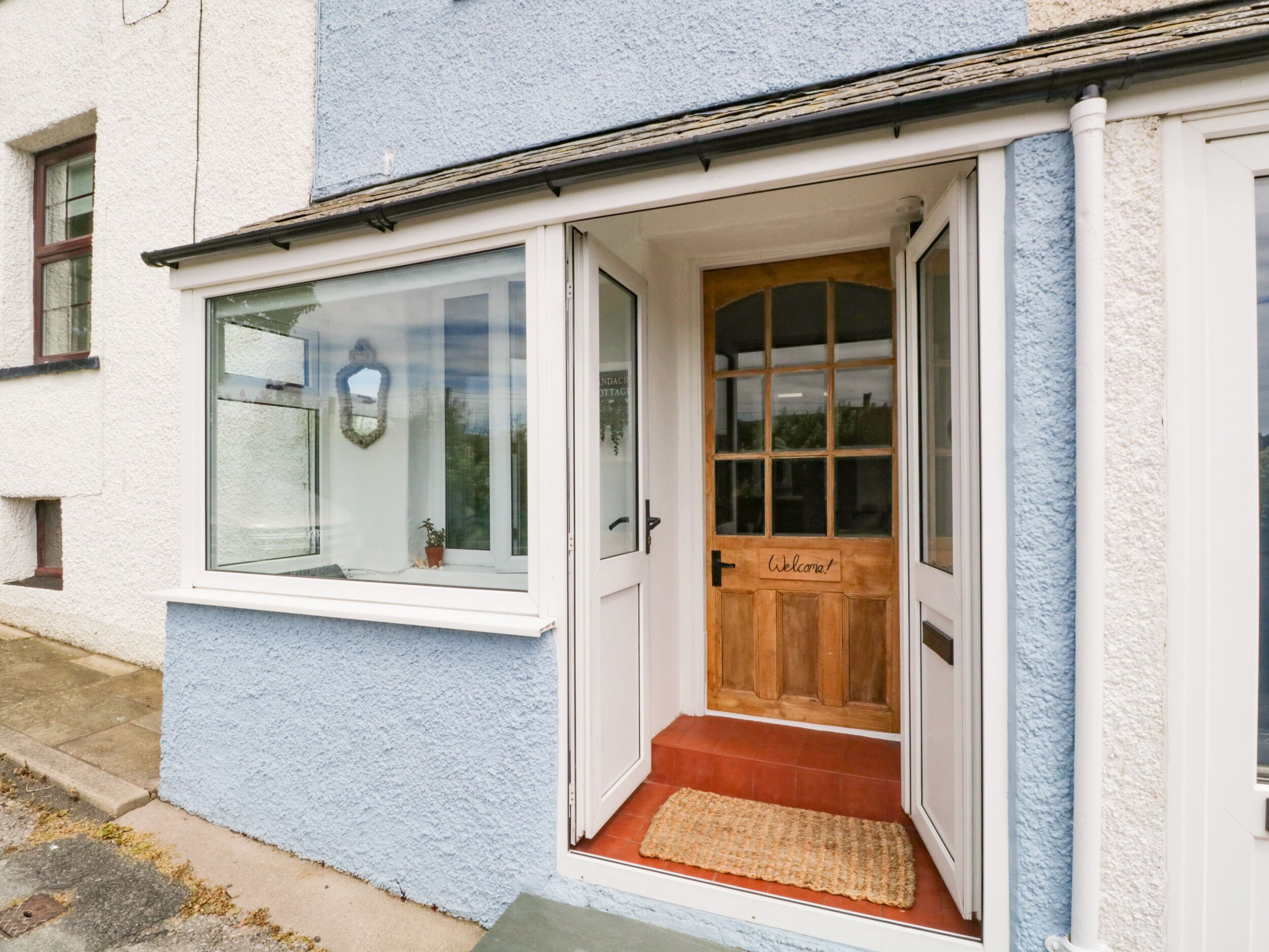 A cottage with a wooden door, a welcome sign, and a small porch area.