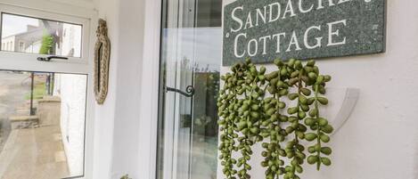 Une enseigne indiquant « Sandacre Cottage », avec une plante suspendue et une petite plante en pot fixée au mur.
