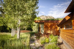 A wooden cabin with a stone pathway leading to the entrance, surrounded by lush greenery and trees.