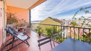 Ein Balkon mit Tisch und Stühlen, einem kleinen Topfpflanzen und Blick auf die Stadt.
