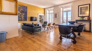 Ein modernes Wohnzimmer mit einer Couch, Fernseher und einem Essbereich mit Stühlen und einem Tisch.