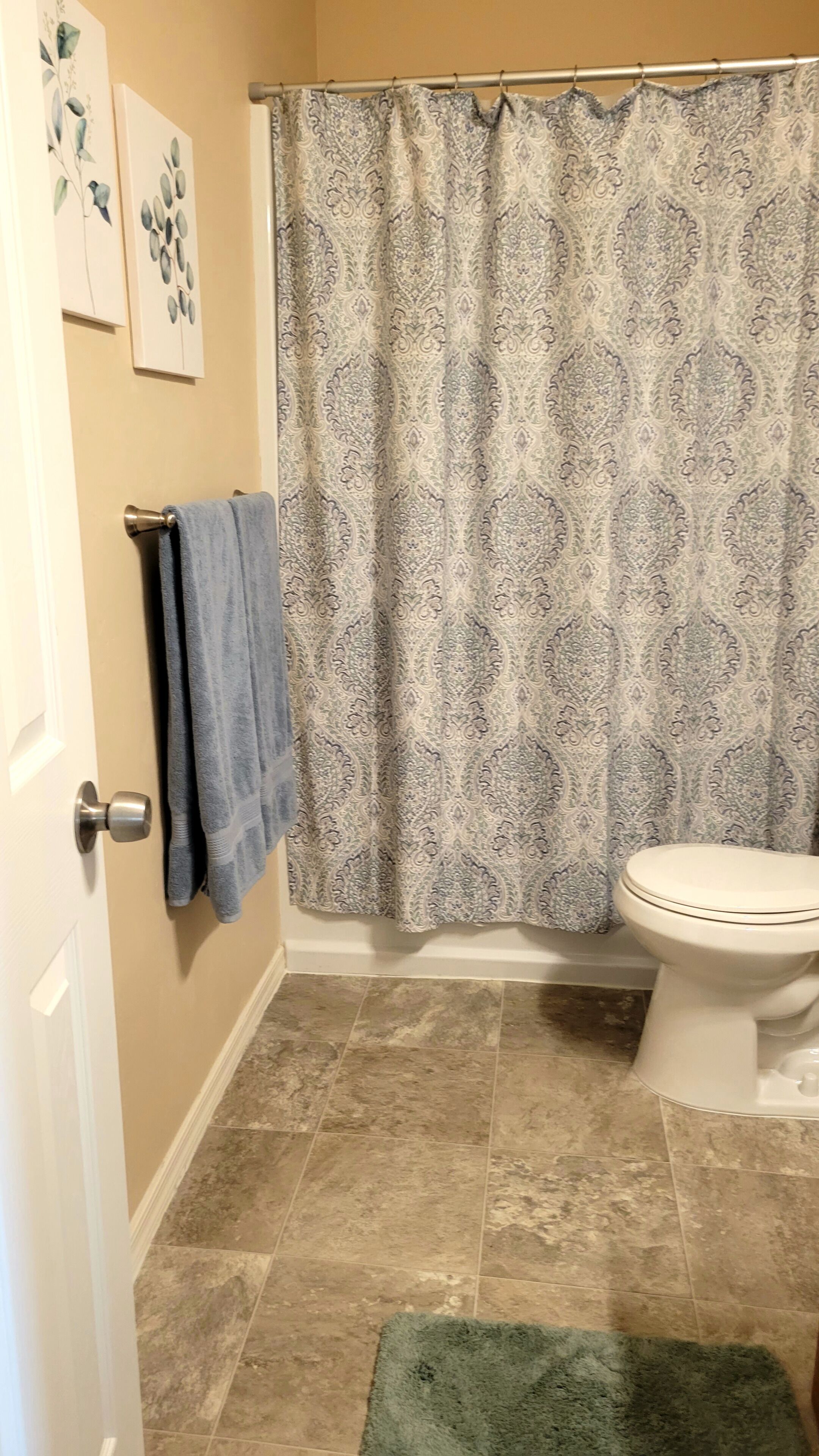 A bathroom with a patterned shower curtain, a toilet, and a towel rack with a blue towel.