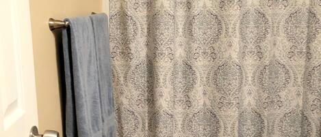 A bathroom with a patterned shower curtain, a toilet, and a towel rack with a blue towel.