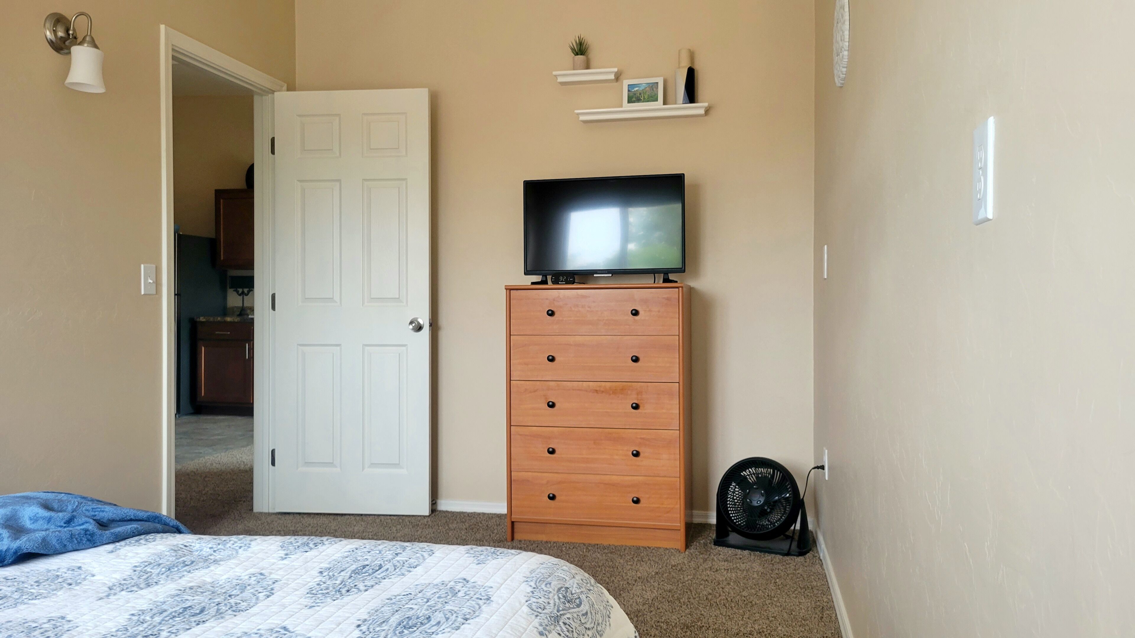 A bedroom with a bed, a dresser, a television, and a fan.