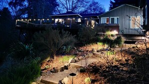 A house with a deck and outdoor lighting, surrounded by trees and a garden.