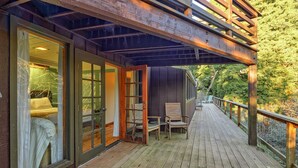 A wooden deck with a covered area, a chair, and a bed visible through glass doors.