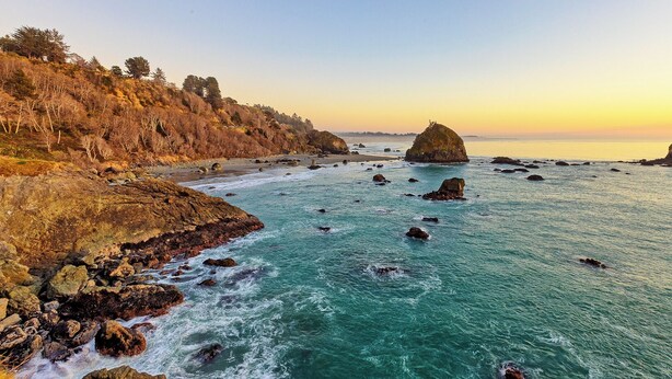 A coastal landscape with rocky shores, clear turquoise waters, and a sunset.