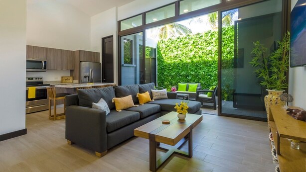 A modern living room with a sofa, coffee table, and a view of a lush green garden through large glass doors. - New! Beachside Casa Yara - Beautiful Villa, Jaco Beach (Jaco)