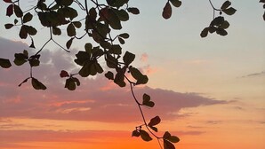 A sunset over a beach with a calm sea and a person walking along the shore. - New! Beachside Casa Yara - Beautiful Villa, Jaco Beach (Jaco)