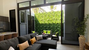A modern living room with a black sectional sofa, a wooden coffee table, and a glass door leading to a patio area with outdoor furniture. - New! Beachside Casa Yara - Beautiful Villa, Jaco Beach (Jaco)