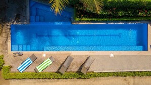 A rectangular swimming pool with clear blue water, surrounded by a brick walkway. There are four lounge chairs with striped towels, and a palm tree is visible in the background. - New! Beachside Casa Yara - Beautiful Villa, Jaco Beach (Jaco)