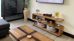 A modern living room with a flat-screen TV mounted on the wall, a wooden coffee table, a sofa, a large potted plant, and a sliding glass door leading to another room. - New! Beachside Casa Yara - Beautiful Villa, Jaco Beach (Jaco)