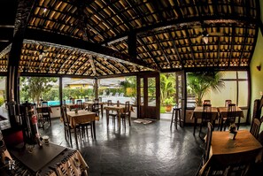 An indoor dining area with a thatched roof, tables, chairs, and a view of a pool outside. - Pousada Da Ferradura (Búzios)