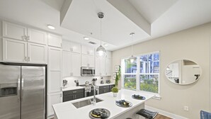 Una cocina moderna con armarios blancos, electrodomésticos de acero inoxidable, una isla central con pileta y un amplio ventanal con vista a la ciudad.