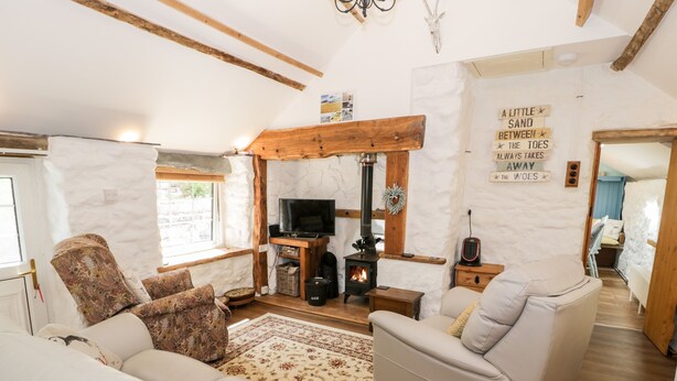 A cozy living room with a stone wall, wooden beams, a fireplace, a television, and comfortable seating.