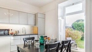Una cocina moderna con armarios blancos, una mesa de comedor con sillas negras y vistas al jardín a través de un amplio ventanal.