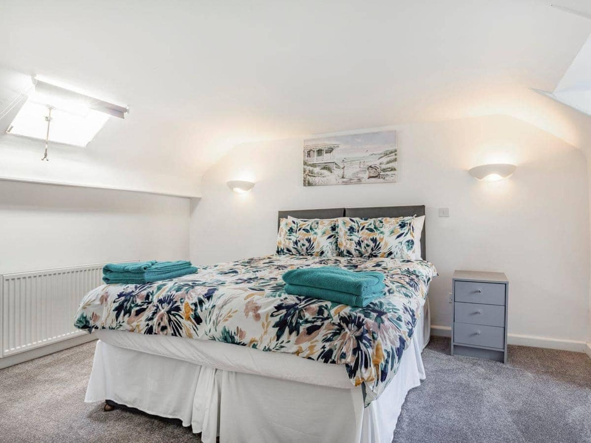 A bedroom with a bed, a nightstand, a radiator, and a wall-mounted light fixture.