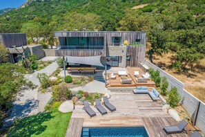 Una villa moderna con piscina, mobiliario exterior y vistas a las colinas circundantes.