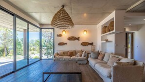 A modern living room with a large window, a sofa, a coffee table, and decorative fish wall art. - Superb Villa with pool, sea & maquis views. Terrace 400m from the beach! (Sainte Lucie de Porto-Vecchio)
