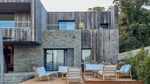 A modern outdoor deck with wooden furniture and stone accents. - Superb Villa with pool, sea & maquis views. Terrace 400m from the beach! (Sainte Lucie de Porto-Vecchio)