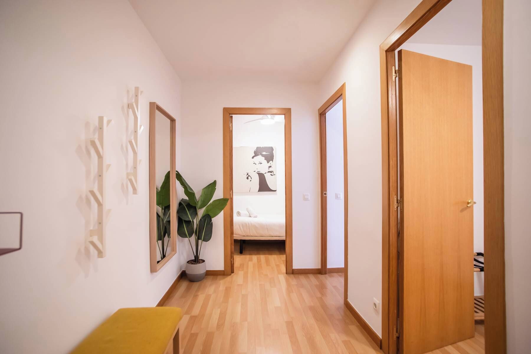 A hallway with a bed in the background, a potted plant, and a yellow chair.