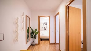 A hallway with a bed in the background, a potted plant, and a yellow chair.
