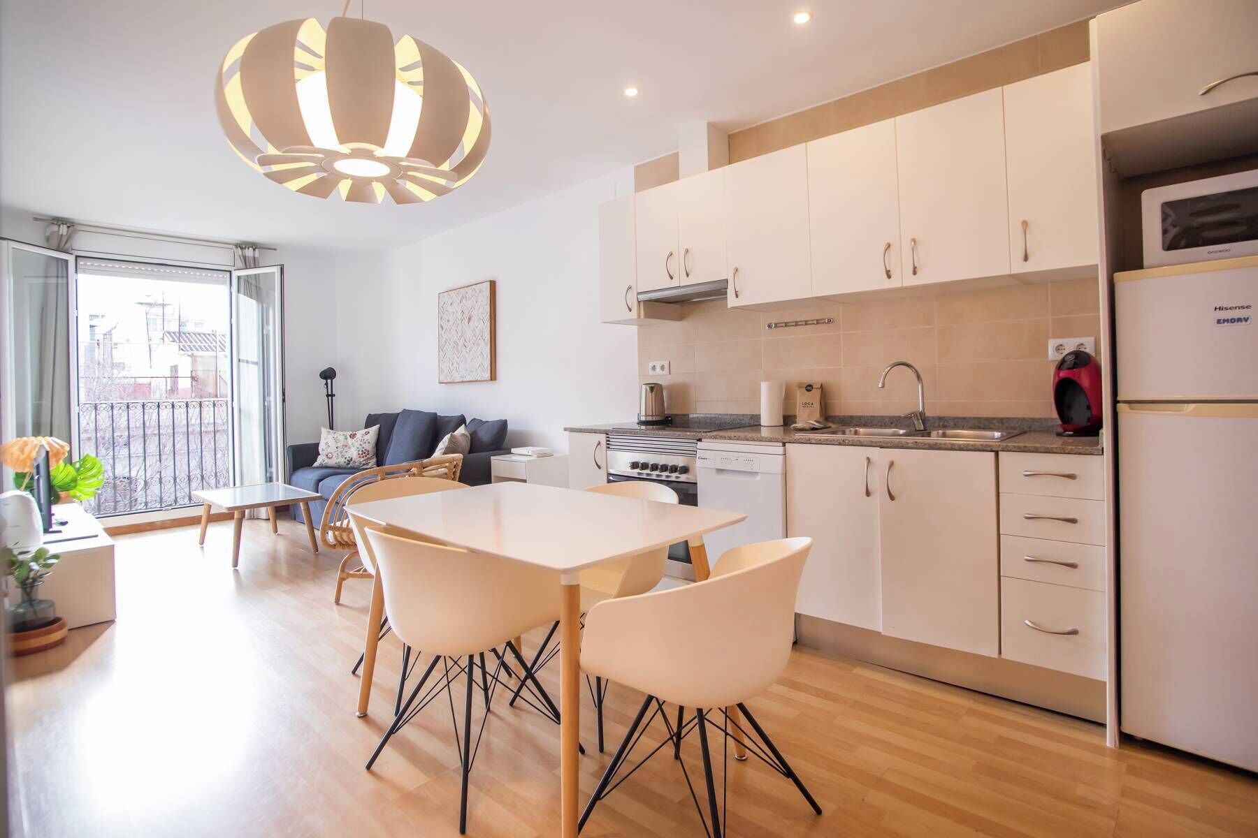 Eine moderne Küche mit weißen Schränken, ein Essbereich mit Tisch und Stühlen sowie ein Balkon mit Blick.