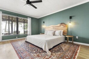 Um quarto com uma cama grande, um ventilador de teto, uma mesinha de cabeceira e uma janela com persianas.