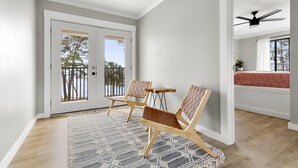 Une pièce spacieuse dotée d’une grande porte-fenêtre coulissante donnant sur un balcon, de deux chaises en bois, d’un tapis à motifs et d’un ventilateur de plafond.