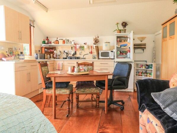 A compact kitchen with wooden cabinets, a dining table with chairs, a microwave, and various kitchen utensils. - Detox Dunchideock (Exeter)