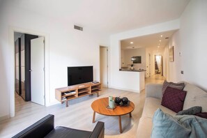 A modern living room with a flat-screen TV, a wooden coffee table, a sofa, and a dining area in the background.