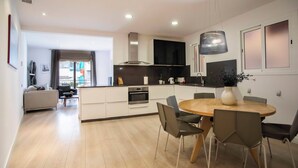 Een moderne keuken met een eethoek, met een ronde houten tafel en stoelen, een ingebouwde oven en een grote hanglamp.