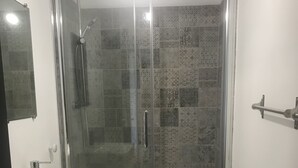 A bathroom with a glass-enclosed shower, a white sink, and a wooden table. - Semi-detached apartment with land (Cauneille)