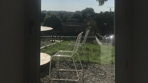 A view through a doorway with a metal chair and a table outside, a clear sky, and a distant building. - Semi-detached apartment with land (Cauneille)