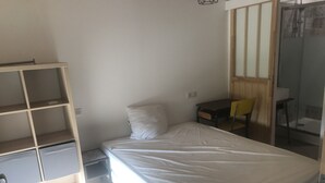 A small, sparsely furnished room with a single bed, a desk, a chair, and a shelving unit. - Semi-detached apartment with land (Cauneille)