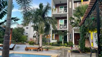Un edificio moderno de varios pisos con piscina, mobiliario exterior y abundante vegetación.