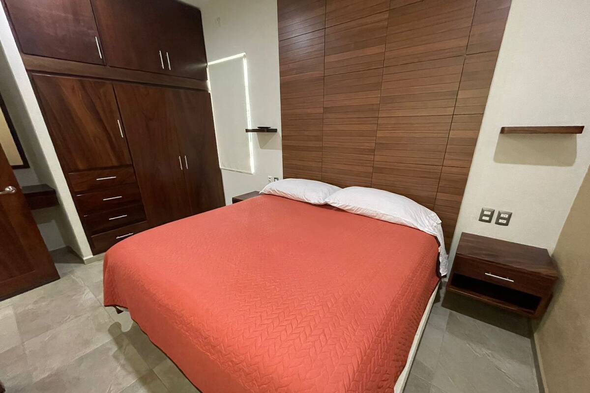 A bedroom with a bed, wooden wardrobe, and a nightstand.