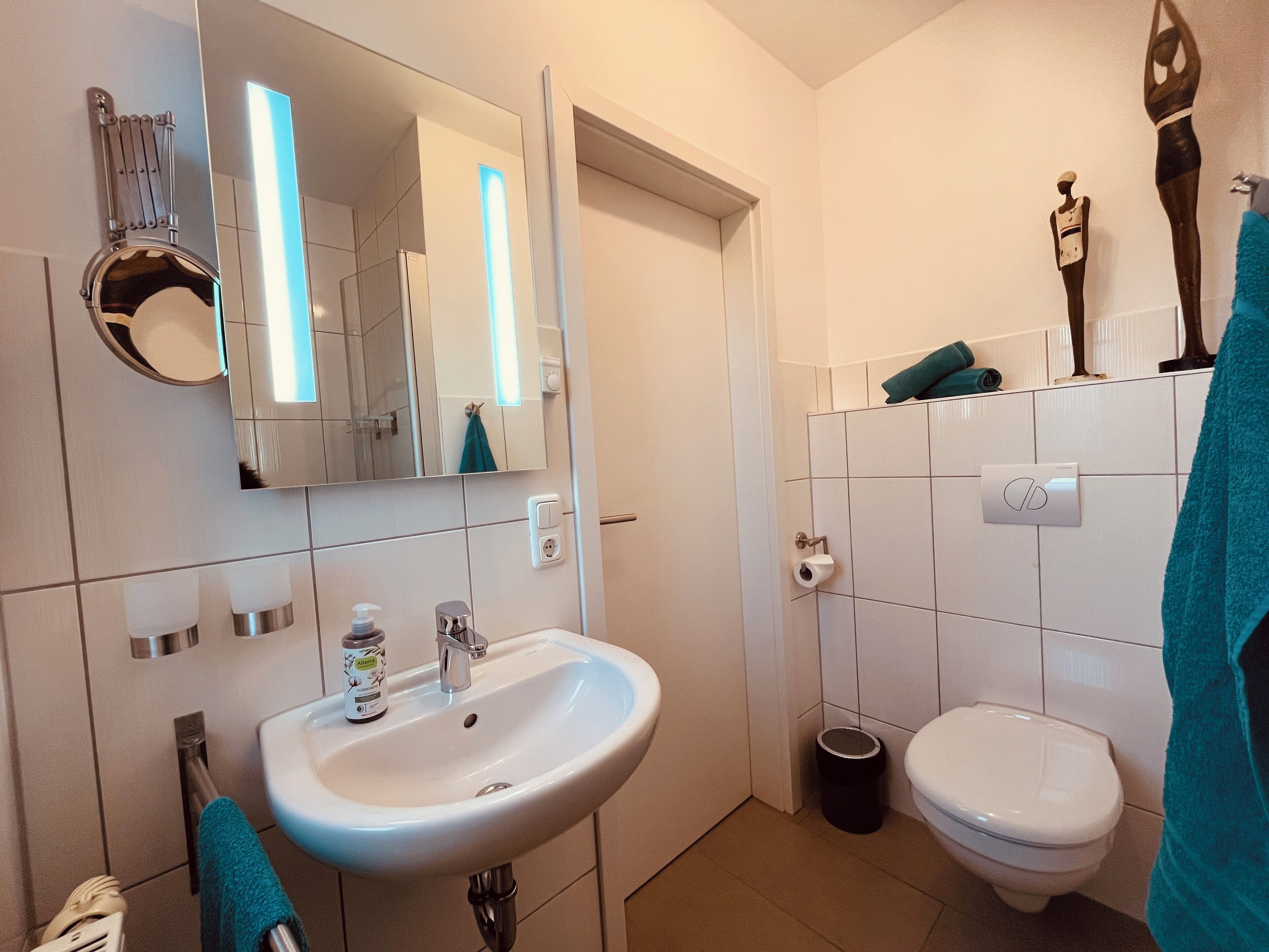 Une salle de bain avec un lavabo, des toilettes et un miroir. On y trouve des serviettes et une poubelle.