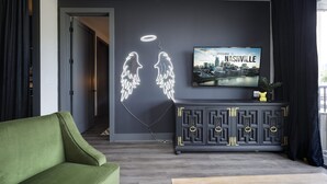 Un salon moderne avec un canapé vert, un meuble sombre orné de motifs décoratifs et une décoration néon représentant un ange, accrochée au mur.